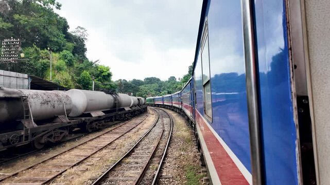 Local train slowly moving past chemical freight tank trains on a railway track in Sri Lanka.