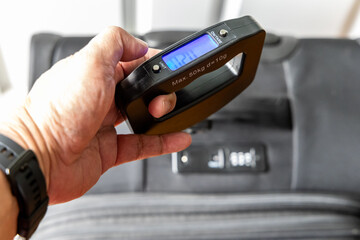 Perspective view of hand holding digital weighing scale to ascertain luggage weight compliant before travel by air