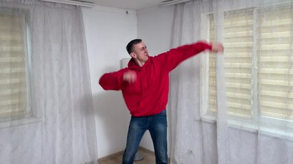 Man in casual clothing performs a repetitive dance move in a bright room, showcasing energy and creativity