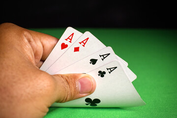 close up of adult hand holding four aces poker cards on green table for background