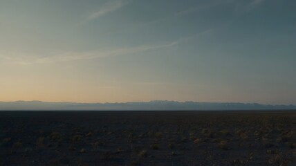 Vast desert plain with distant mountain range under soft sunset light