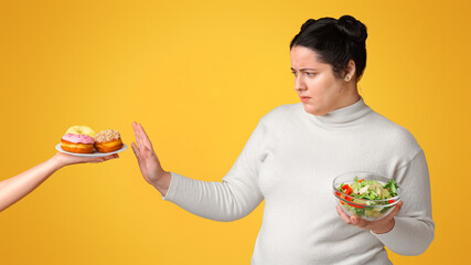 Healthy life concept. Young plump girl refusing junk food, holding bowl with vegetable salad,...