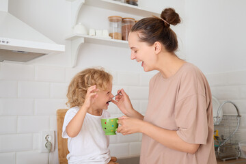 Joyful laughing little girl and her mother having fun in kitchen while enjoying healthy snack together expressing happiness during warm family time