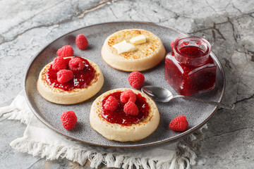 Hot fresh breakfast crumpets with butter melting, jam and fresh raspberries closeup on the plate on the table. Horizontal