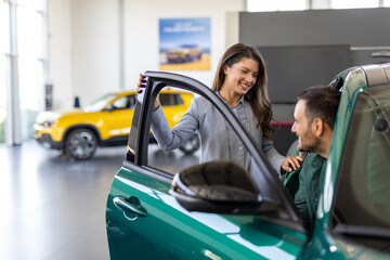 Happy middle age businessman buying new and luxury car. Beautiful female dealer helps him to make...