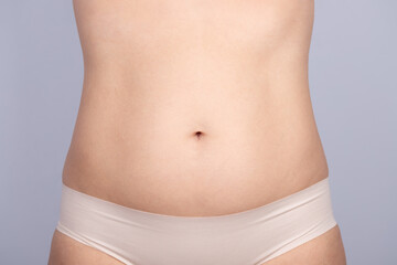 Close-up close-up of a woman's belly in underwear and gray background. Concept of woman, skin and belly