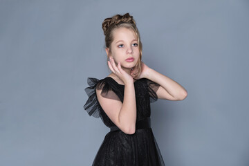 A girl in a formal black dress gently frames her face with her hands, embodying grace and beauty....