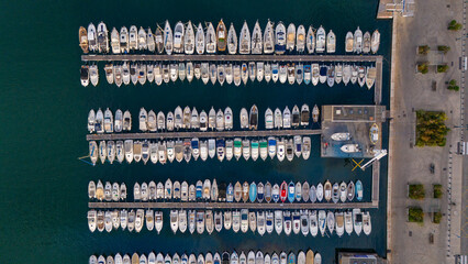 Aerial view of a marina in Marseille, France, with boats and yachts docked in neat rows along the waterfront. The deep blue water contrasts beautifully with the vessels. 