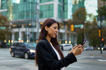 Fototapeta premium Hispanic businesswoman using mobile phone on a city street with tall buildings in the background