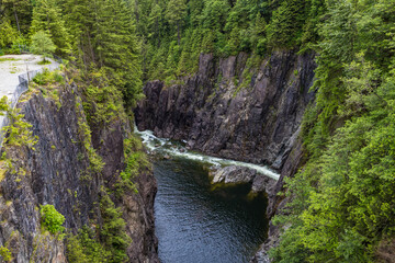 A dramatic canyon at Cleveland Dam in North Vancouver, featuring steep rock walls and a flowing river below, surrounded by lush green forest