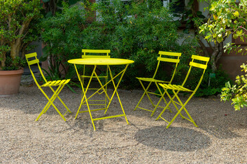 A yellow metal table and four chairs sit in a garden, ready for a relaxing outdoor meal