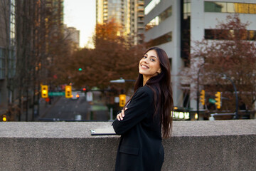 Obraz premium Smiling young businesswoman standing in front of a modern building with autumn foliage