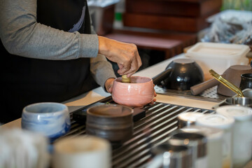 Woman whisking matcha powder while making matcha green tea with traditional accessories for tea ceremony