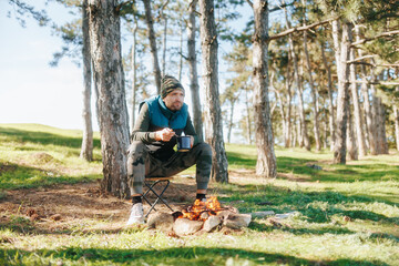 Seated Next to a Campfire, a Man Eats from a Pot in the Forest