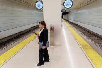 Businesswoman in Suit Typing on Phone While Waiting at Train Station Platform