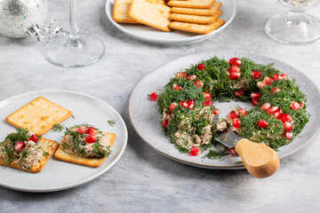 Tuna pate decorated with dill and pomegranate seeds. Christmas salad in shape of Christmas wreath served with crackers.