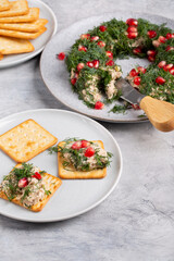 Tuna pate decorated with dill and pomegranate seeds in shape of wreath served with crackers.