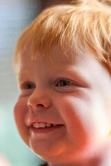 A cheerful young boy with bright red hair is captured smiling widely and happily in a warm and inviting setting