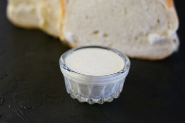 Delicious homemade mayonnaise sauce. Mayonnaise in a glass saucer and appetizing white bread on a dark table