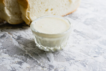 Delicious homemade mayonnaise sauce. Mayonnaise in a glass saucer and appetizing white bread on a light table