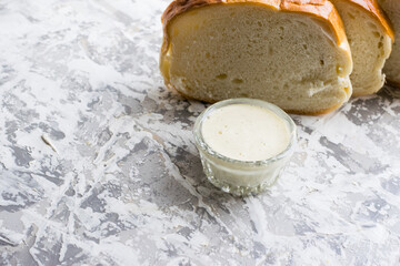 Delicious homemade mayonnaise sauce. Mayonnaise in a glass saucer and appetizing white bread on a light table