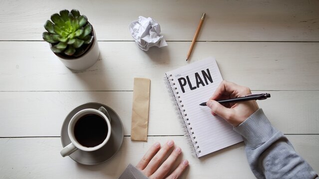 White table with coffee, a succulent, and someone writing Plan in a notebook