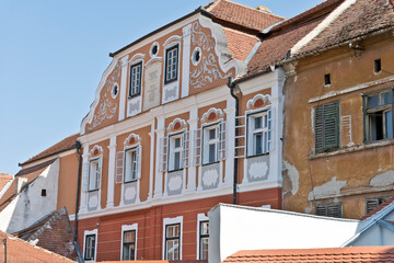A colorful facade of a historic building in Sibiu, Romania. There is a plaque with Latin inscription and the name "JOHANNES GEORGA SOHAGER" above the windows.