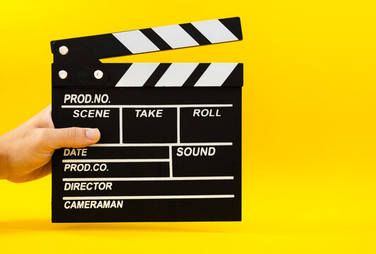 Male hand holding a black wooden film clapperboard on a yellow background, production and cinema concept