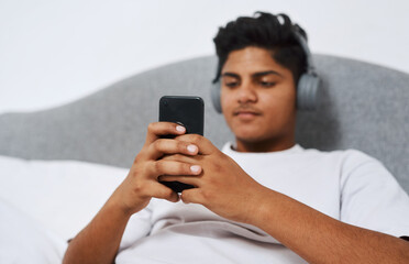 Teenager, headphones and person with phone in home for network, connection and listening to song. Calm, boy and relax with technology in bedroom for audio, streaming and update of music playlist