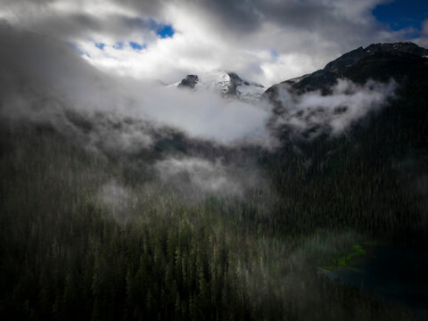 Aerial view of a majestic forest shrouded in fog with dramatic mountains and clouds, Agassiz, Canada.