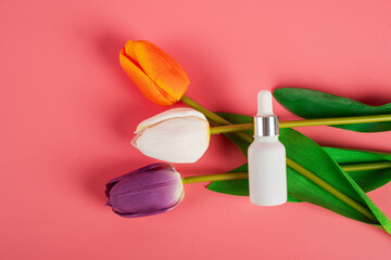White sunscreen bottle with stylish props and colorful tulips on pink background. Sunscreen concept. Skin care concept. Copy space.