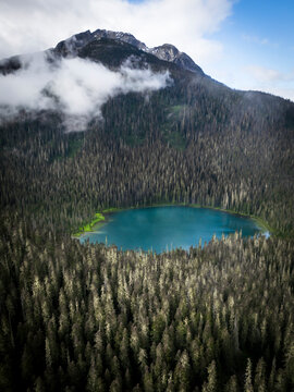 Aerial view of tranquil forest and serene lake under clouds with majestic mountains, Agassiz, Canada.