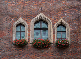 three gothic windows on a red brick wall with flower pots
