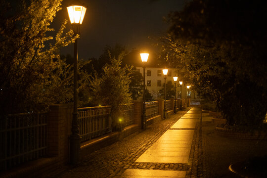 Fototapeta night cityscape after the rain, lanterns at night along the pedestrian path after the rain with the reflection of light on the path