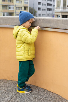 Offended 5 year old boy in an autumn yellow jacket and blue hat, standing sad, upset, sadness, sadness, emotional stress