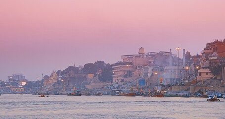 Varanasi, Uttar Pradesh, India. Many Boats Moored On Ganga River Near Ghats. Hundreds Of Tourists And Locals Come In Boats To Watch Ganga Maha Aarti Ceremony And Fire Ceremony. Purple Sunset Sky At