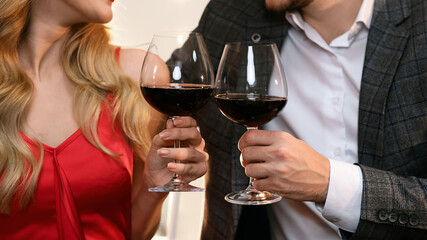 Cheers. Closeup of glasses with red wine in hands of happy couple on date in restaurant, romantic pair celebrating Valentine's day together, crop