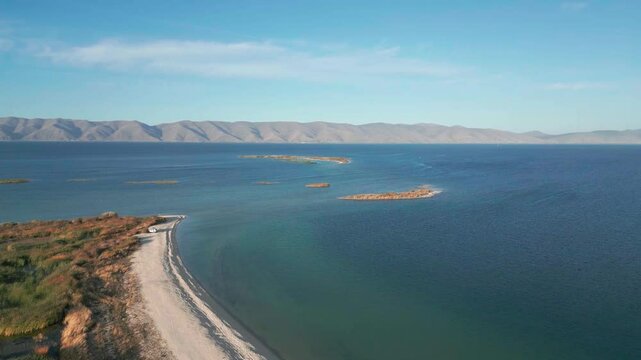 Drone footage mountain lake. Aerial view on Sevan lake in Armenia, West Asia. Aerial shot Beach with grass, blue lake with mountains  background. Tourism in  Caucasus. Wild adventure. Discovery Asia