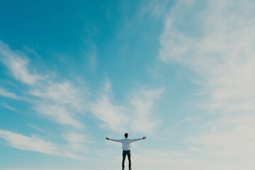 A person stands with open arms under a vast blue sky filled with clouds during a calm and serene afternoon. With copy space for text.