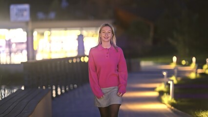 Fototapeta premium A young woman leisurely strolls along a beautifully illuminated waterfront path during the enchanting evening