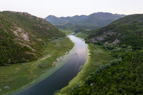 Aerial view of a picturesque winding river surrounded by lush greenery and majestic mountains, Rijeka Crnojevica, Montenegro.