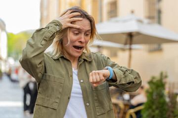 Scared woman worrying to be punctual, with anxiety checking time on watch, running late to work or...