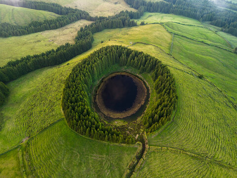 Aerial view of lush Lagoa Pau Pique with surrounding forest and volcanic landscape, Capelas, Portugal.