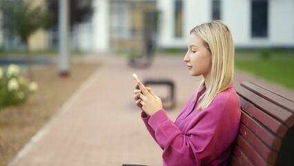 A young woman is completely engrossed in her smartphone while comfortably sitting on a bench in a...