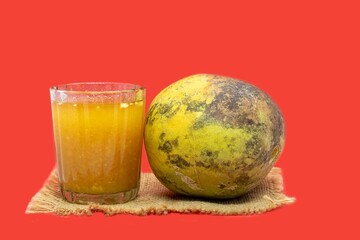 Ripe Indian Bael Fruit Juice or Sharbat in a Glass or Wood Apple on Isolated on Red Background with Copy Space, Also Known as Aegle Marmelos, Bengal Quince, Japanese Bitter Orange or Stone Apple