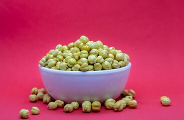 Roasted Garbanzo Bean or Chickpea in a White Bowl Isolated on Red Background with Copy Space, Also Known as Bengal Gram or Egyptian Pea