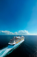 Aerial view of a luxury cruise ship sailing through the ocean under a clear blue sky. 