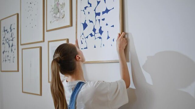 Girl hanging art picture on canvas at modern apartment during relocation closeup