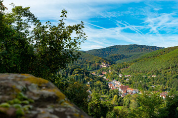 A panoramic view of a small town nestled in a valley, surrounded by lush green hills and a blue sky