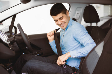 Driving Regulations. Guy Putting On Seat Belt Sitting In New Car In Dealership Center. Selective Focus